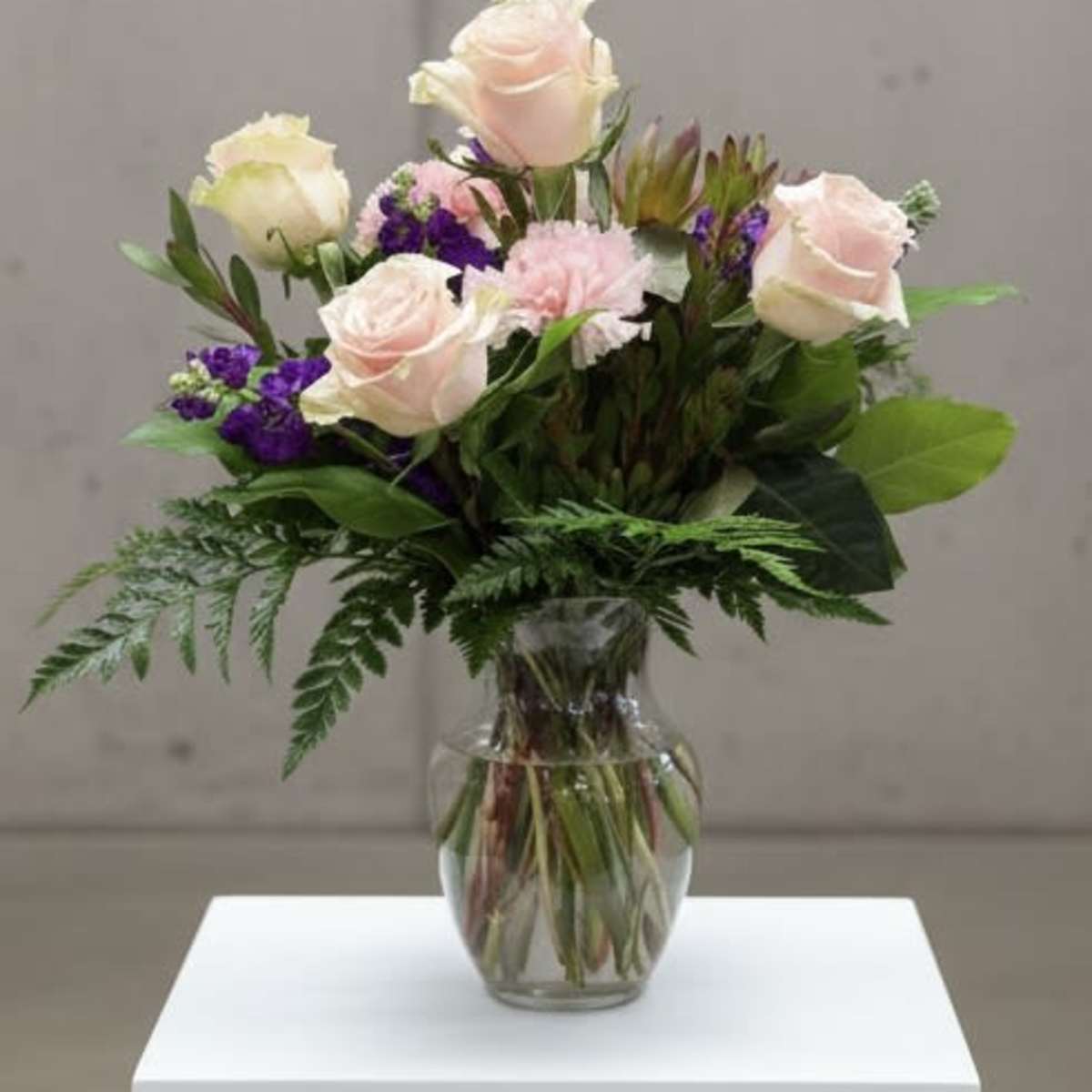 Greenskeeper Florist - Pink roses and purple flowers arranged in a clear glass vase